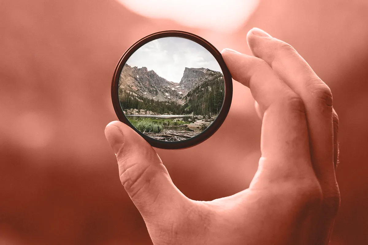 Mano sostiene filtro fotográfico circular con montañas a lo lejos