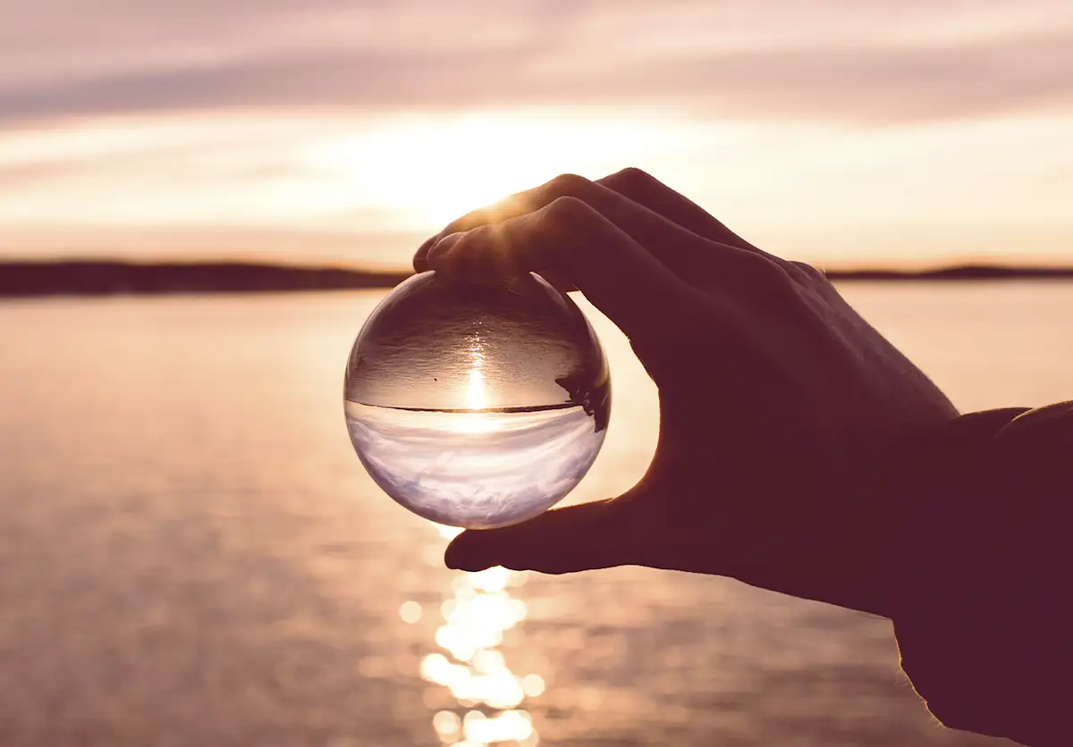 Mano sostiene globo de cristal con vista de lago de fondo